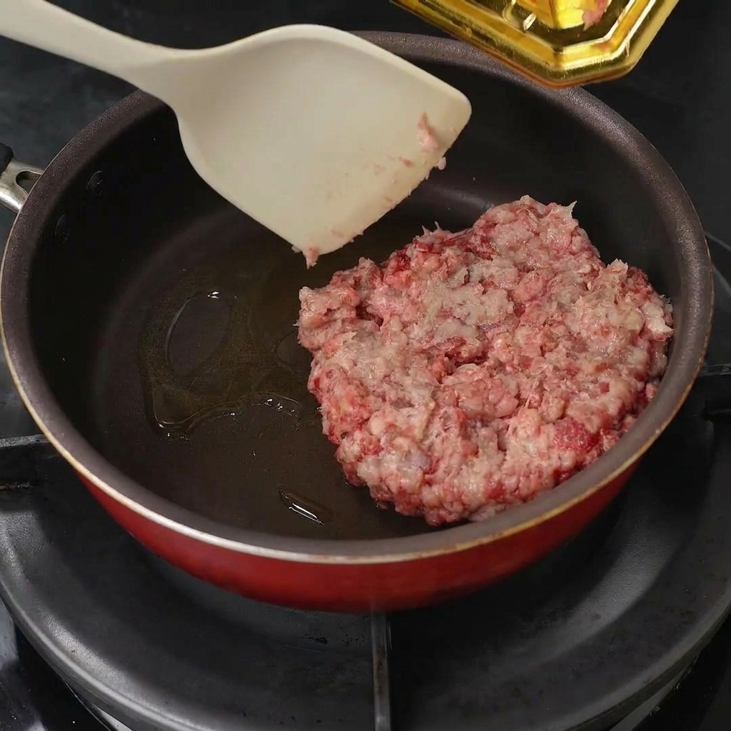 フライパンに入れた牛ひき肉をへらでほぐしている様子。