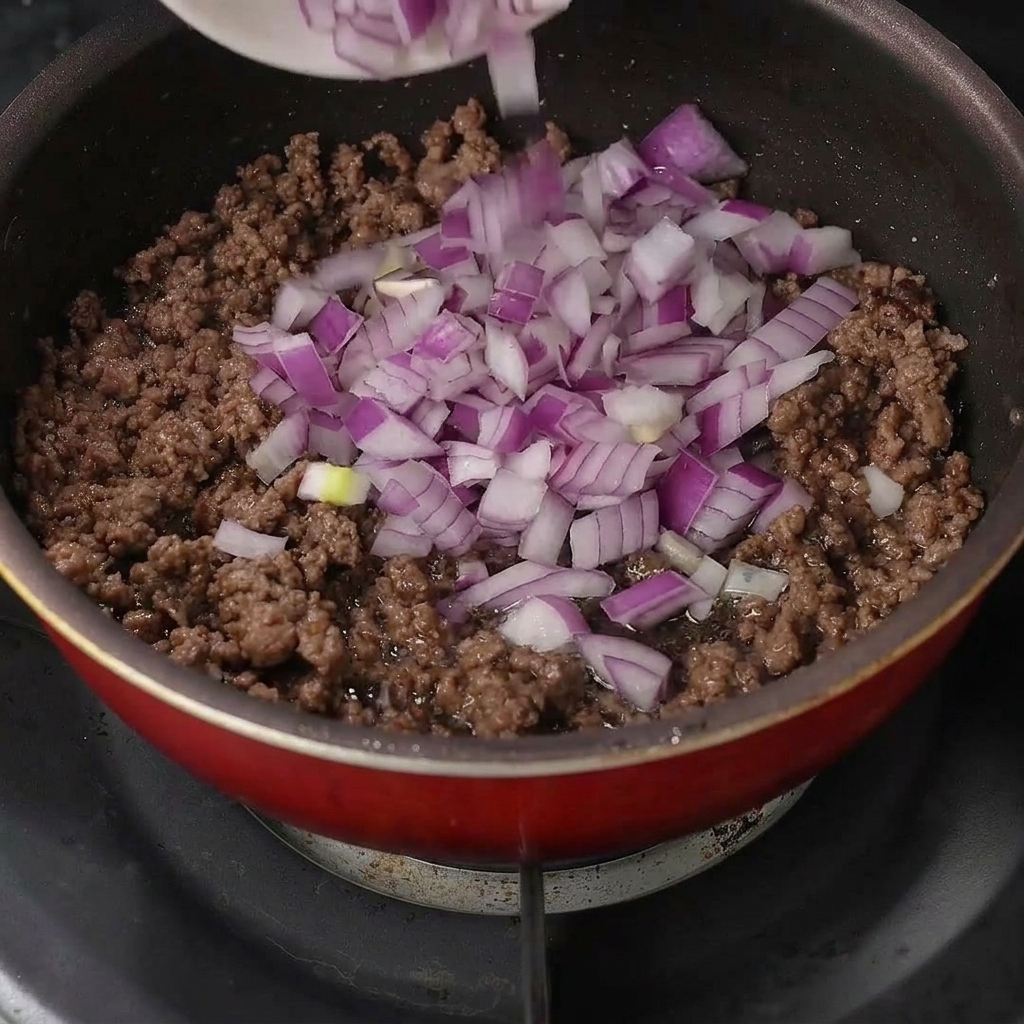 刻んだ紫玉ねぎを炒めた牛ひき肉に加える様子。