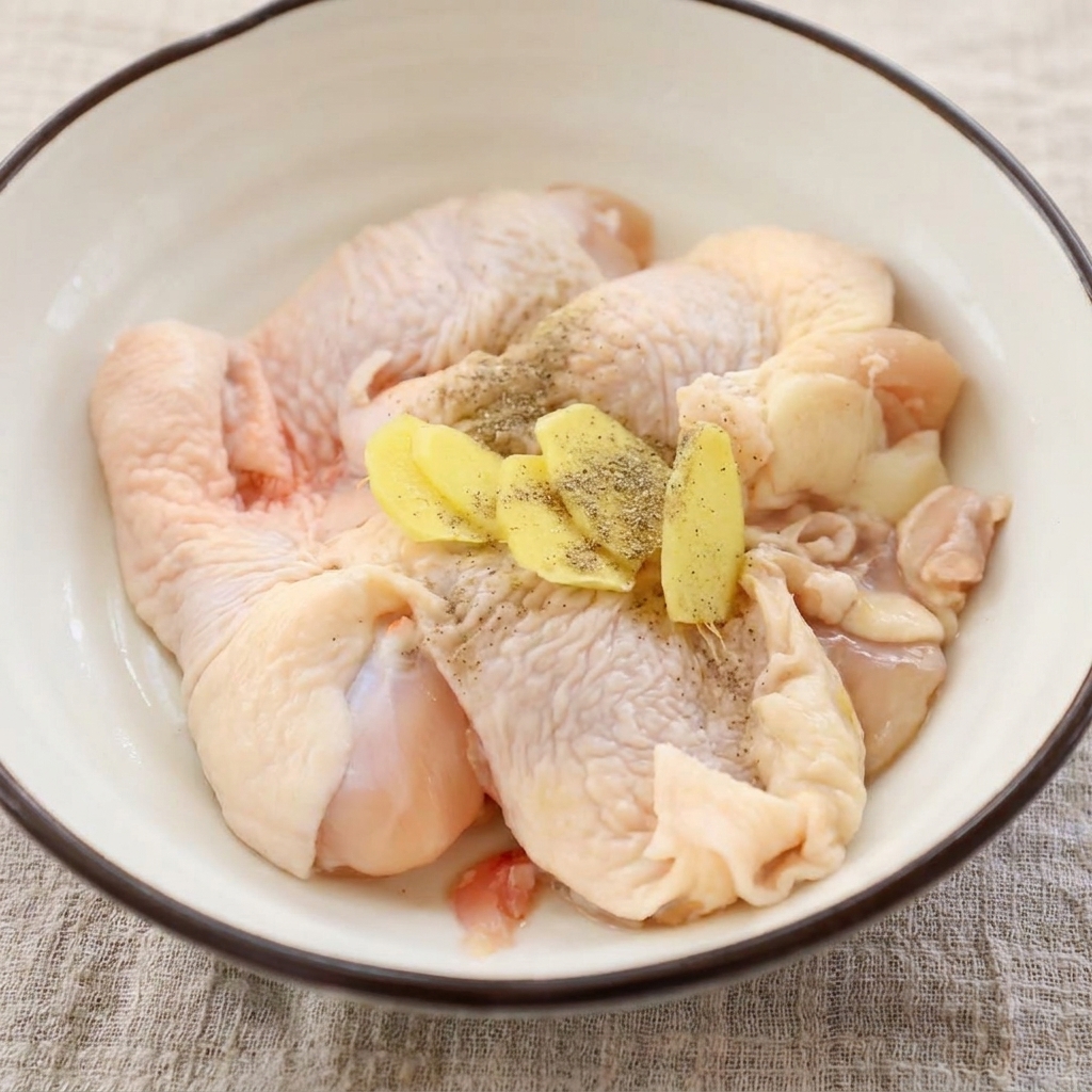 ボウルに入った鶏肉に生姜スライスと黒胡椒が乗っている様子
