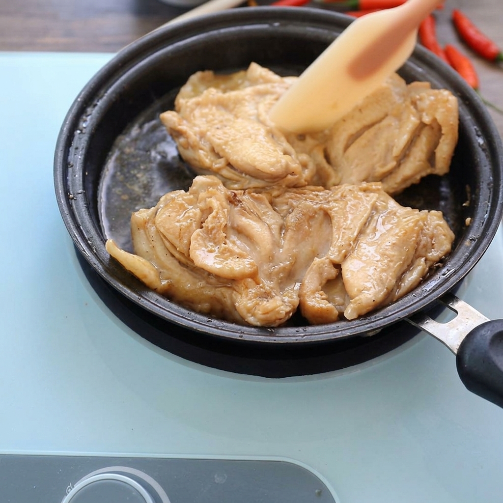 フライパンでタレと鶏肉を煮込み、ヘラで押さえている様子