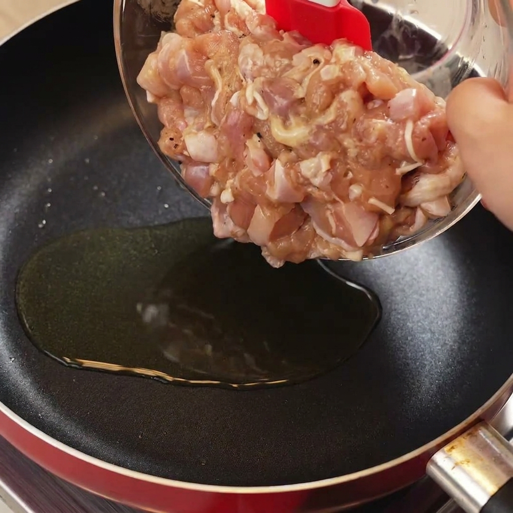 熱したフライパンに鶏肉を入れ、赤いヘラで炒めている様子。