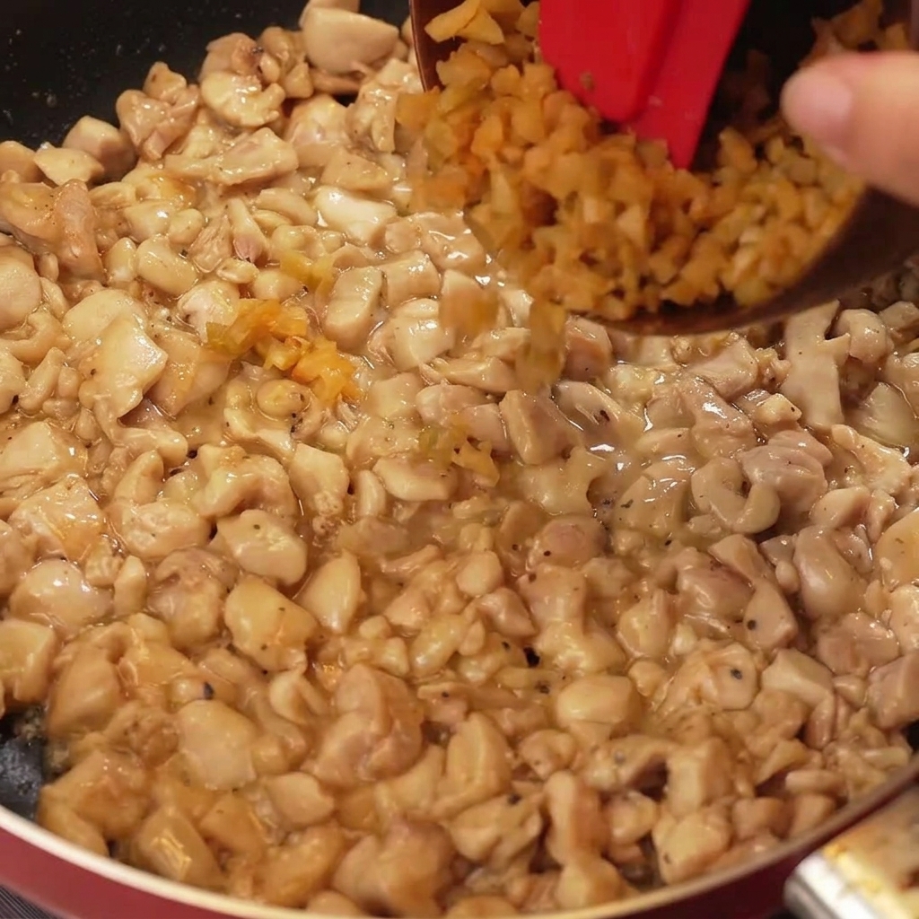 炒めた鶏肉に、刻んだザーサイと青ねぎの白い部分を加えて炒め合わせている様子。