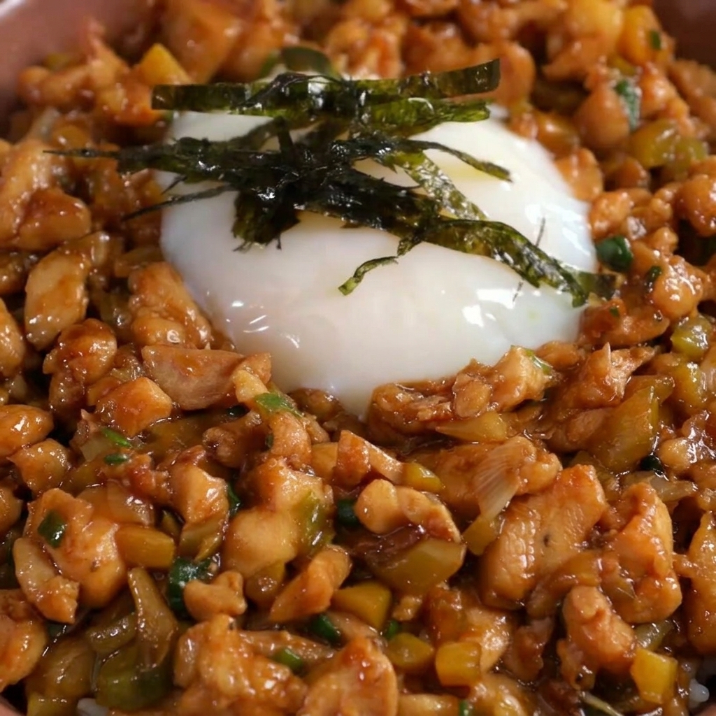 鶏そぼろ丼の中央にのせた温泉卵の上に、細切りの海苔を添えている様子。