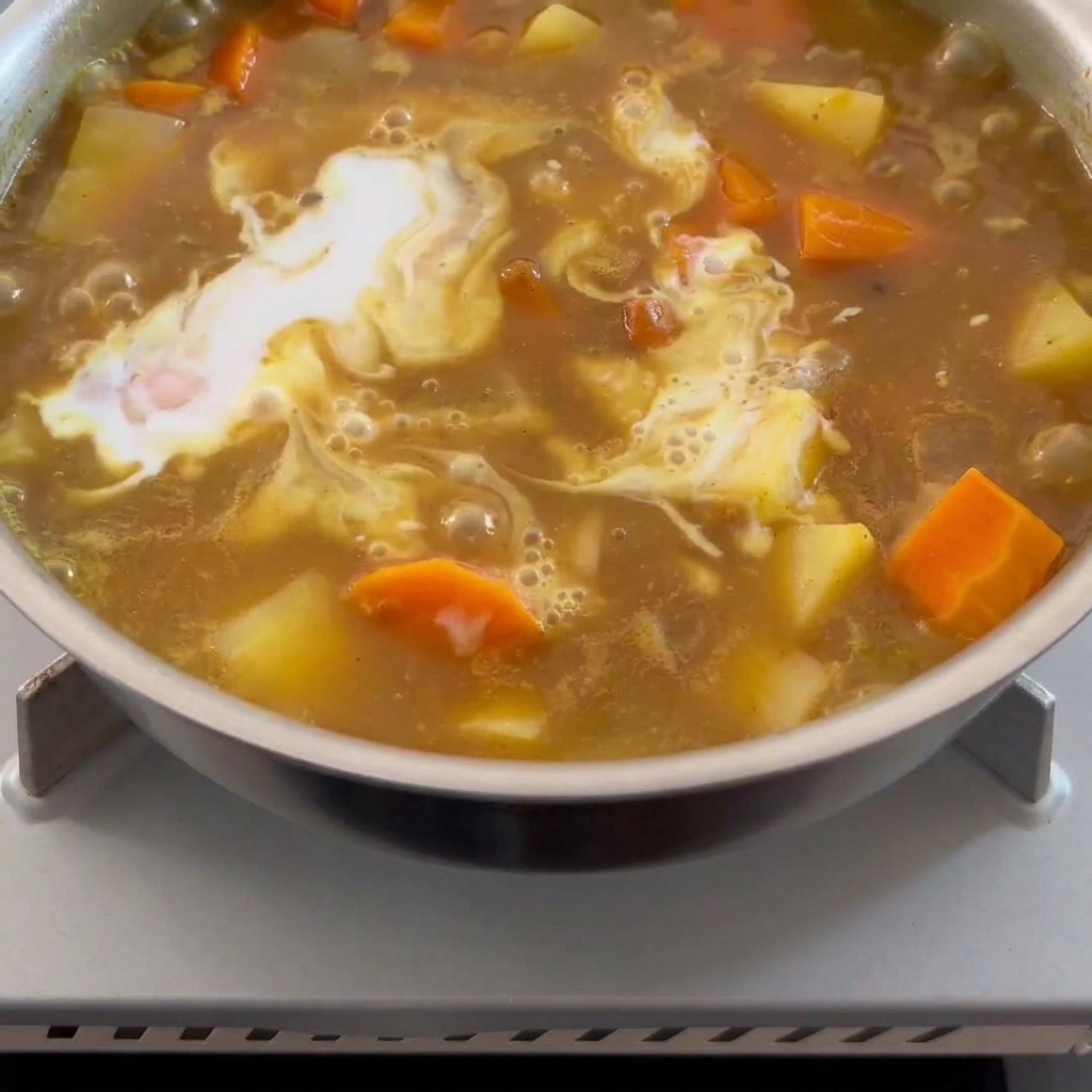 とろみのあるカレーに白いココナッツミルクを回し入れている様子。