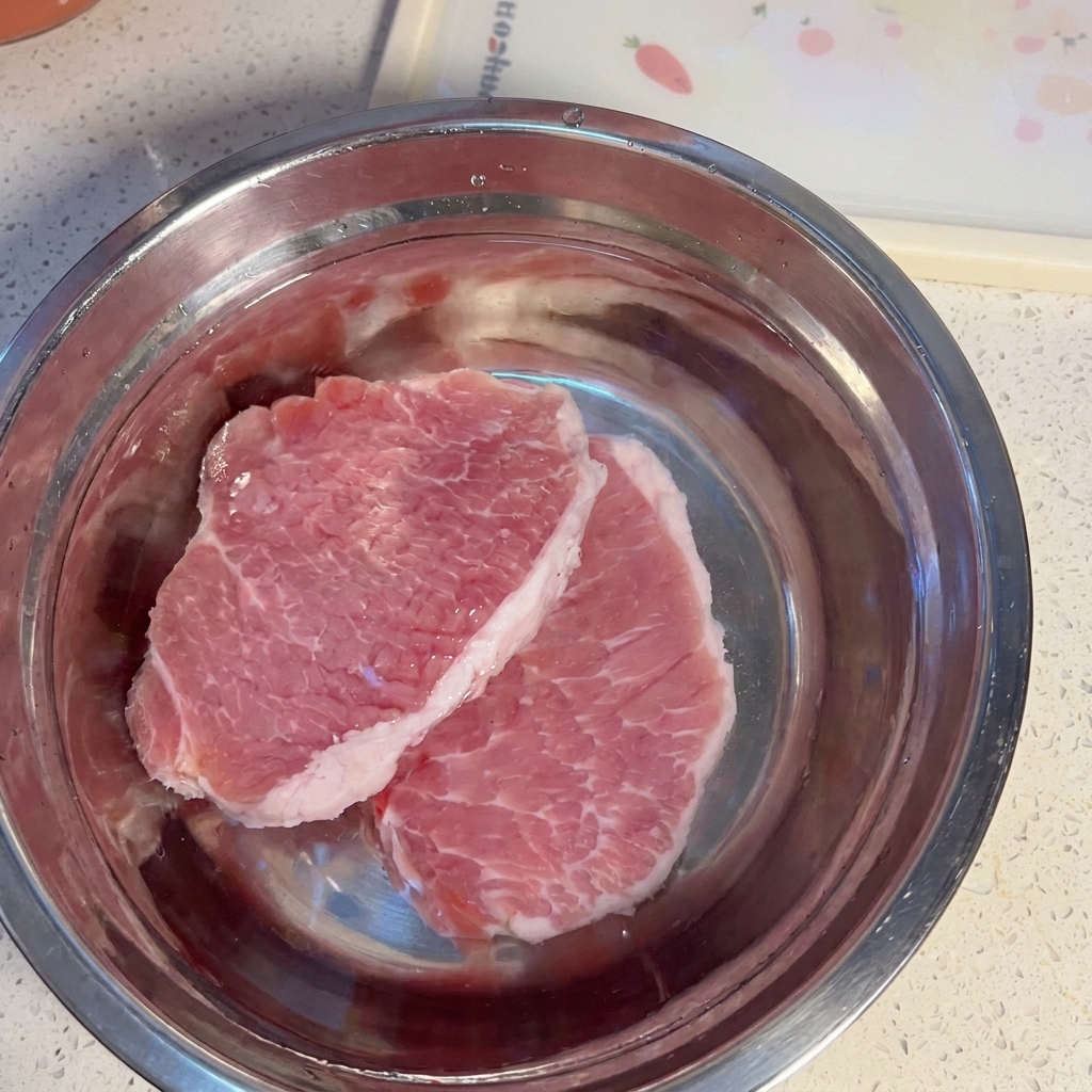 金属製のボウルの中で重曹水に浸かっている豚肉。