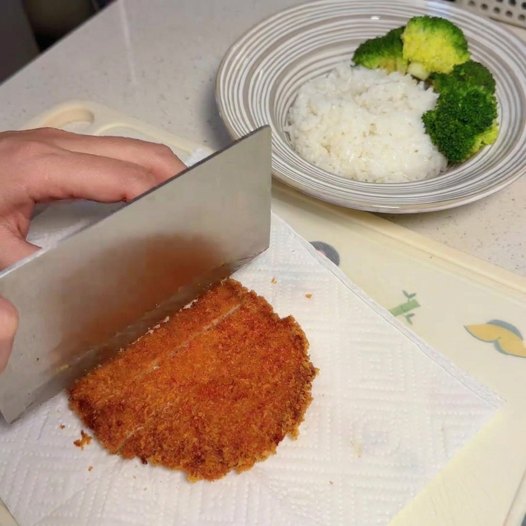 キッチンペーパーの上で揚げたての豚肉を包丁で切っている様子。