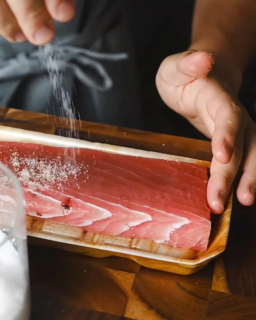 バットにのせた赤い生のマグロの柵に、塩を均等に振っている様子。