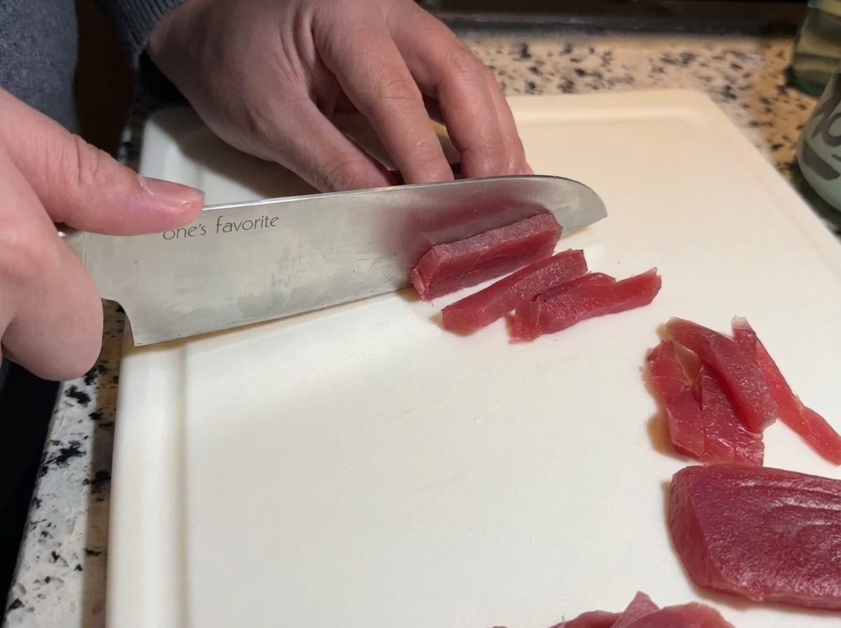 鋭利な包丁で赤身のまぐろを細長くスライスしている様子。