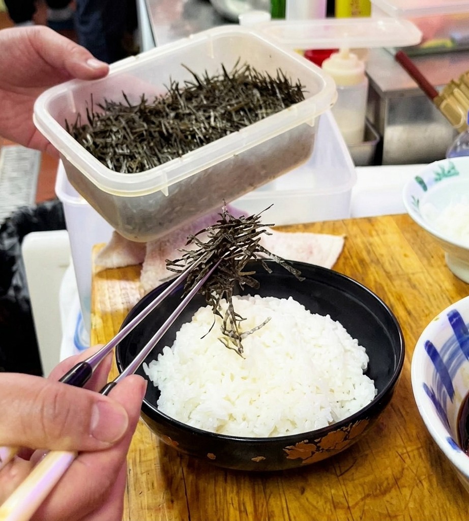 ご飯の上に細切りにした海苔を均等に散らしている様子。