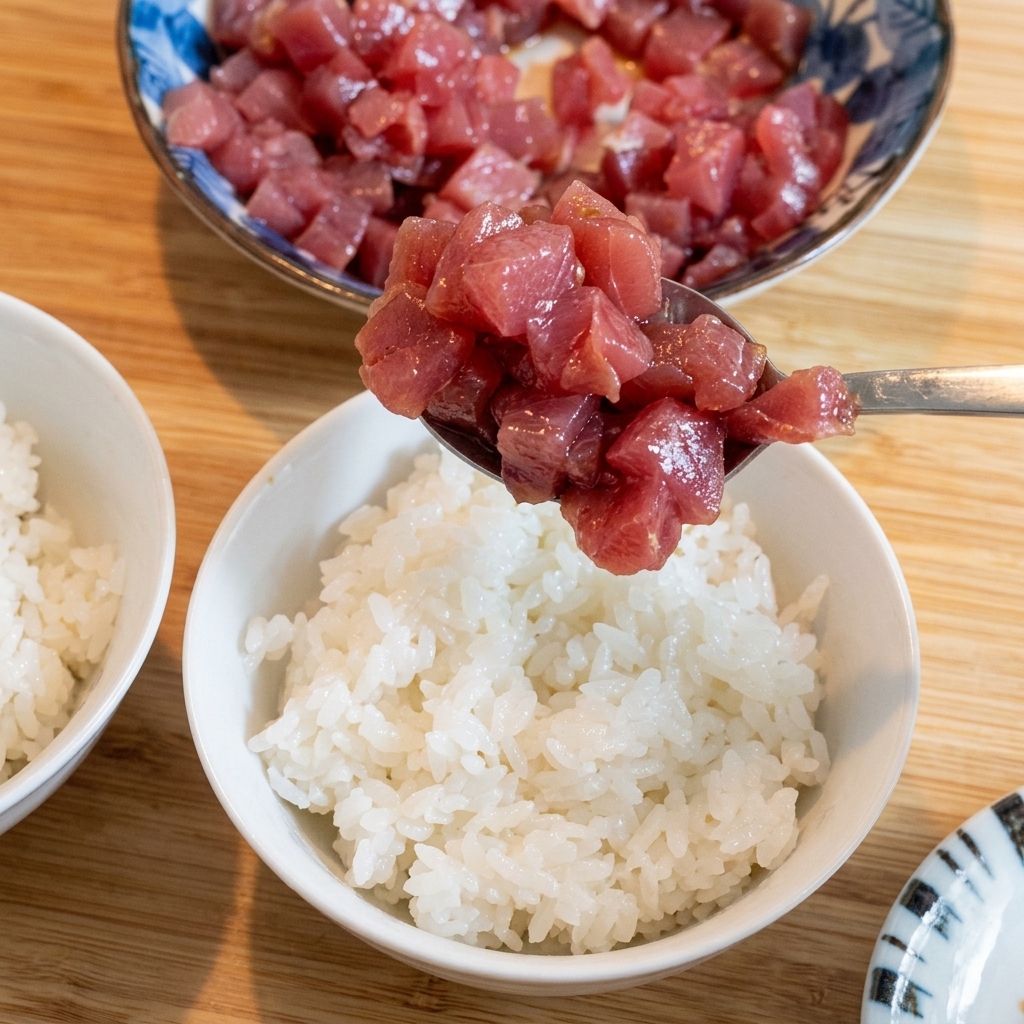 白いご飯の上に、醤油に漬けたマグロを丁寧に盛り付けている様子。