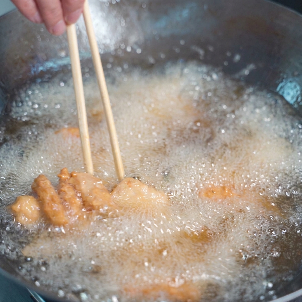 黄金色の油の中で泡を立てながら揚げられている衣付きの豚肉と、それを混ぜる菜箸