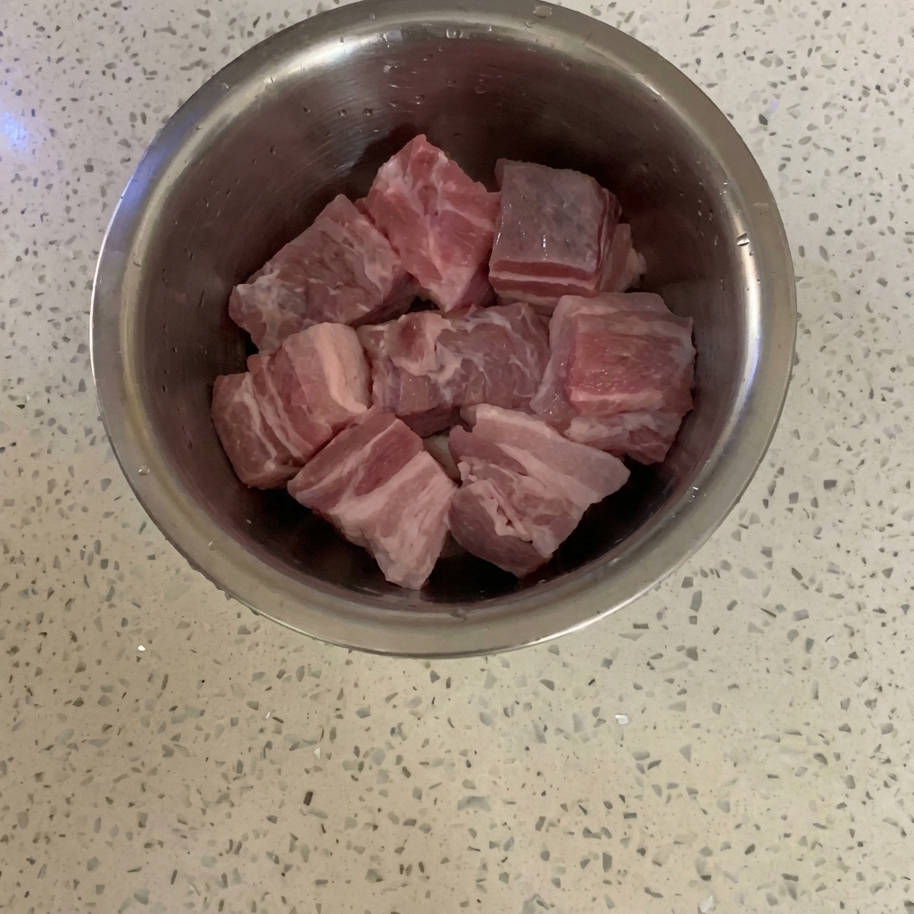 調理台に置かれたステンレス製ボウルに入った、角切りの生の豚バラ肉。