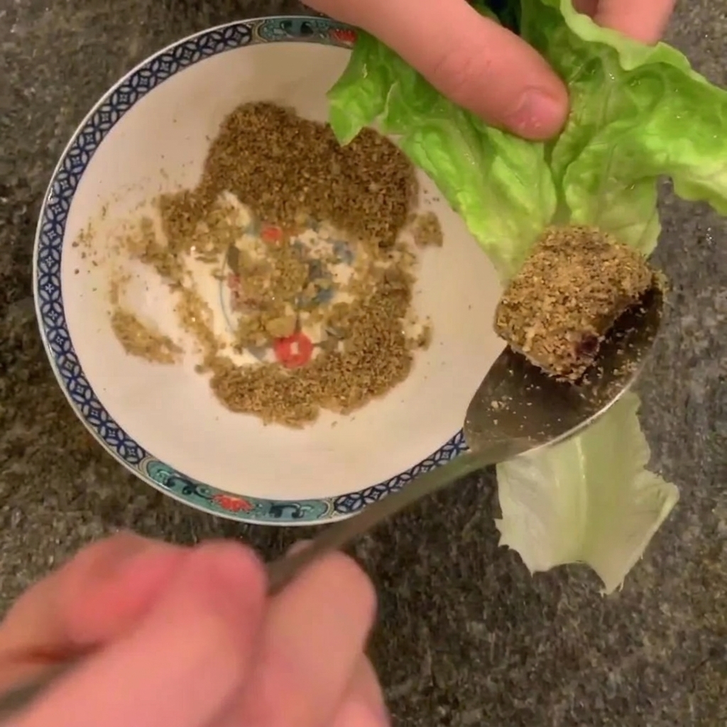 砕いたピーナッツをまぶした豚肉をスプーンですくい、ロメインレタスの上にのせようとしているアップ画像。