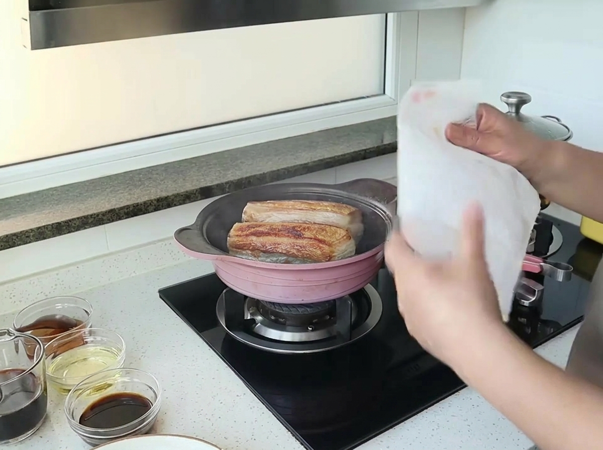 豚肉を焼いているフライパンの上にキッチンペーパーを被せている様子