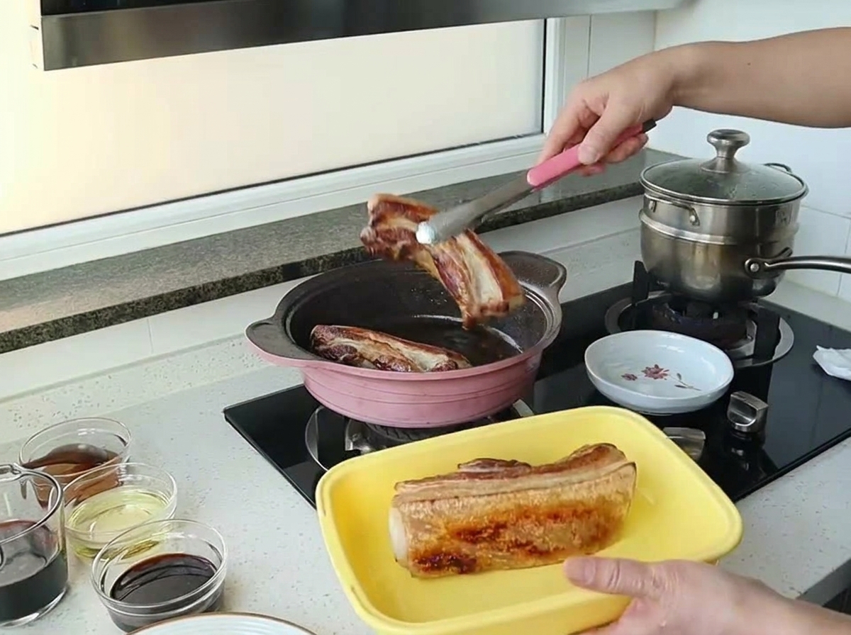 きれいな焼き色がついた豚バラ肉をトングでピンクのフライパンから取り出している様子