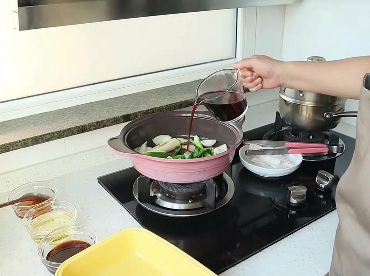 計量カップから赤ワインを、炒めた玉ねぎなどの香味野菜が入ったフライパンに注いでいる様子