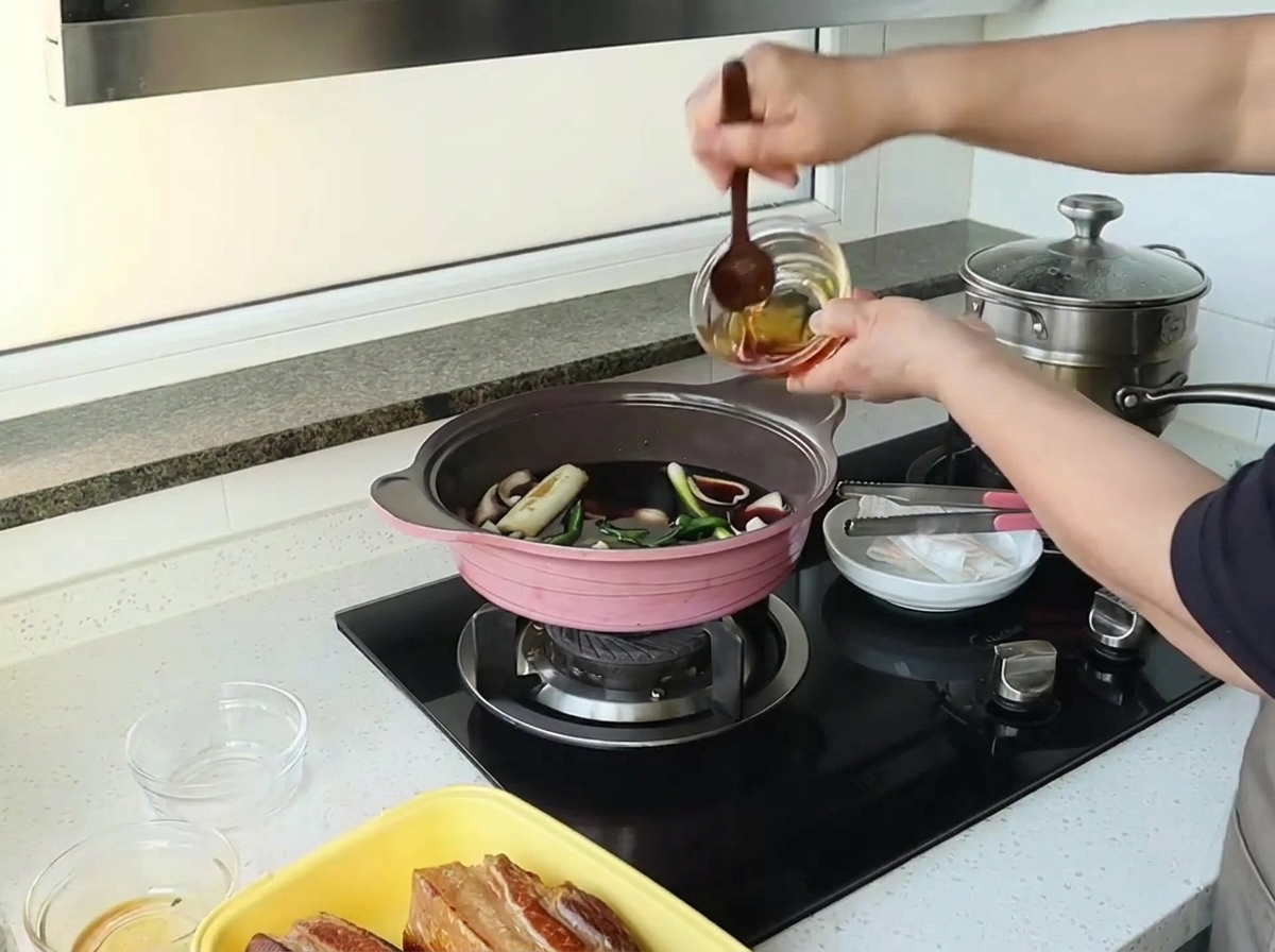 醤油やみりんなどの液体と香味野菜が入ったピンクの鍋に、小さなガラスの器からはちみつを注いでいる様子