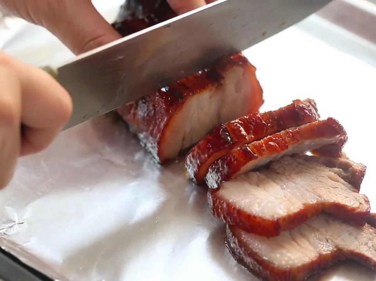 アルミホイルの上に置かれた、照りのある赤ワイン煮込みの豚バラ肉を包丁で切り分けている様子