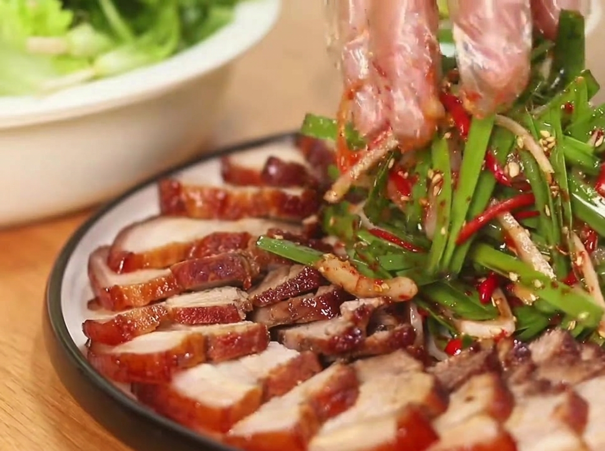 丸いお皿に並べられた豚バラ肉の煮込みの横で、色鮮やかな長ねぎと赤唐辛子のサラダを和えている様子