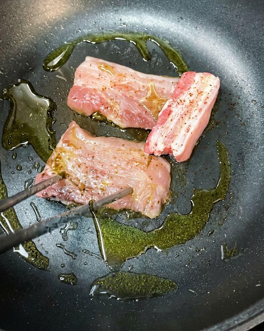 熱したフライパンでオリーブオイルを使い、表面を焼いている豚バラ肉スライス。