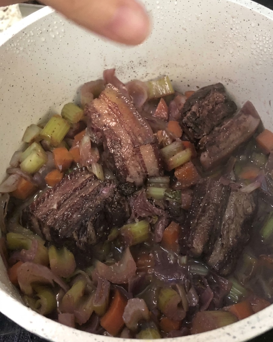 煮込まれた豚バラ肉と野菜の鍋に、黒こしょうを挽き入れている様子。