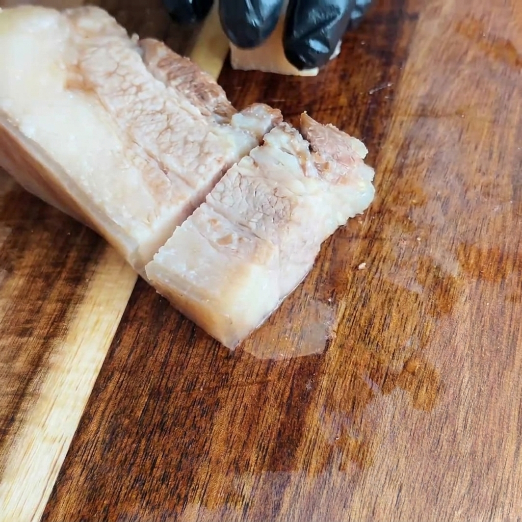 まな板の上で冷めた豚バラ肉を均一な正方形に切っている様子。