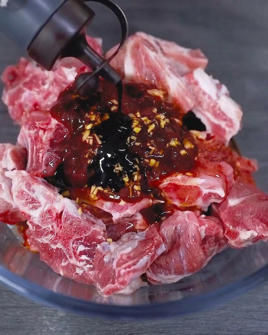 下味をつけたポークリブが入ったガラスボウルに、ボトルから濃口醤油を注いでいる様子。