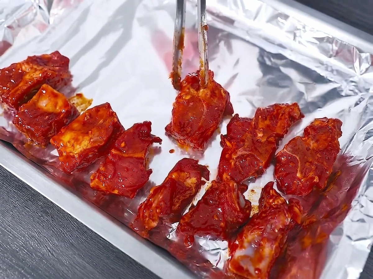 トングを使って、下味をつけたポークリブをアルミホイルを敷いた天板に綺麗に並べている様子。