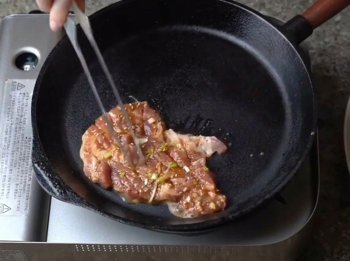 予熱した鉄のフライパンに、漬け込んだ豚肉を並べている様子。