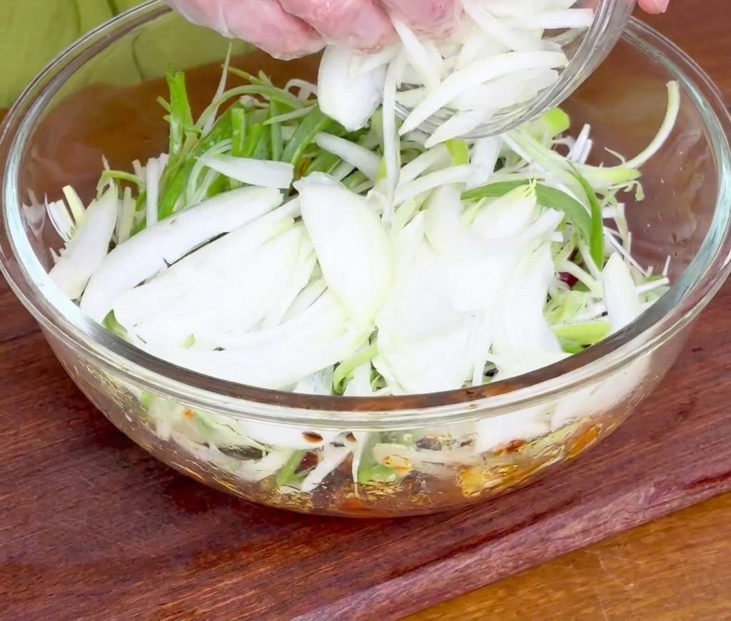 醤油だれに浸かった生の牛肉に、薄切りにした玉ねぎと長ねぎを両手で加えている様子。