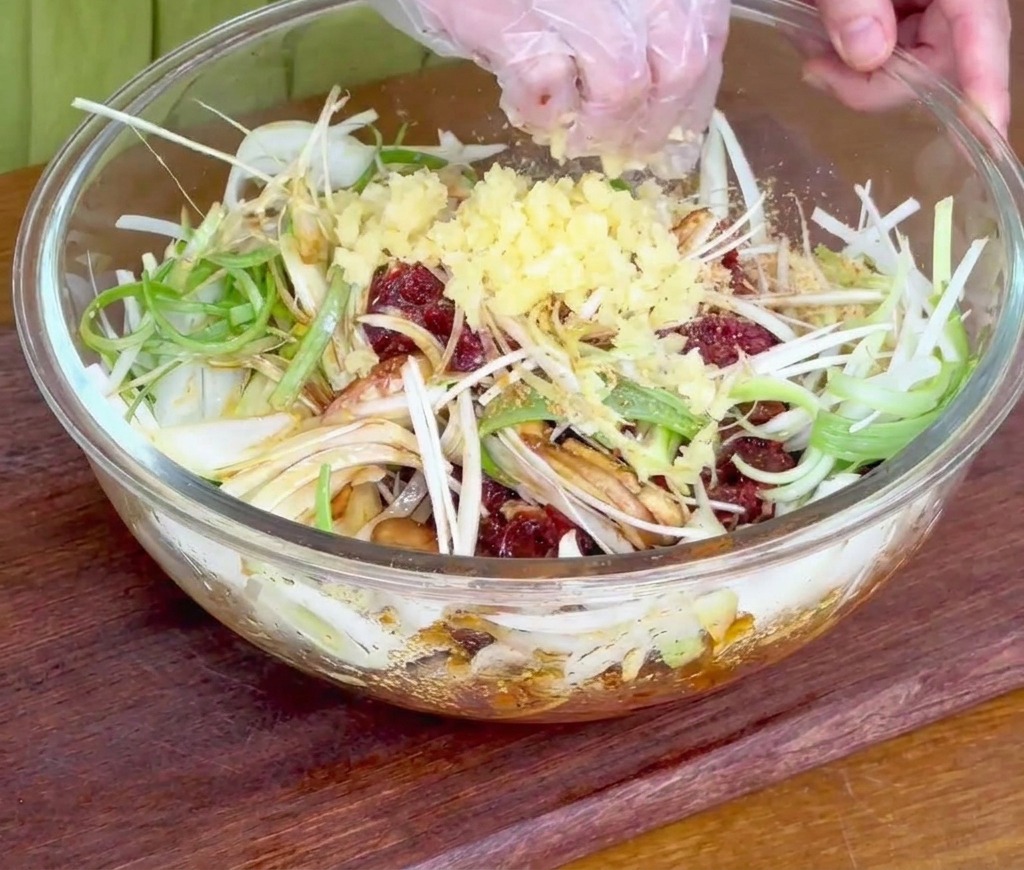 ガラスボウルに入った牛肉と玉ねぎの上に、おろしニンニクを振り入れている手。