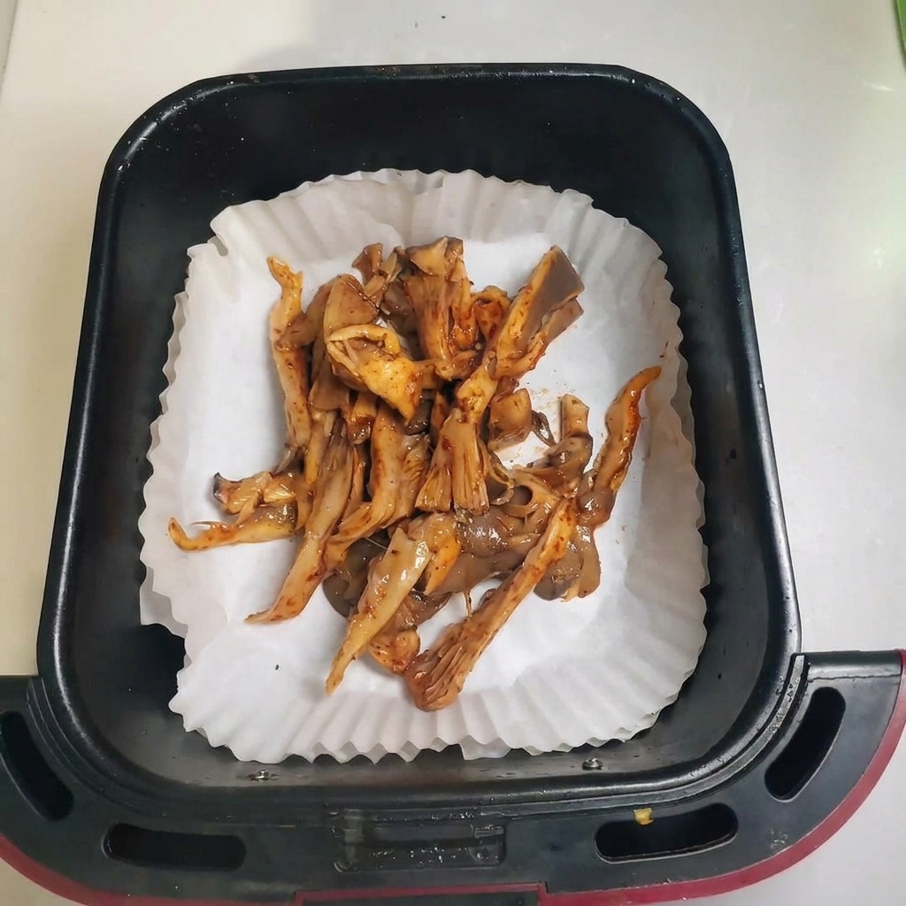 クッキングシートを敷いたエアフライヤーのバスケットに、味付けしたひらたけを広げている様子。