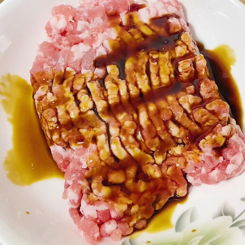 白いボウルに入った豚ひき肉に醤油をかけている様子。