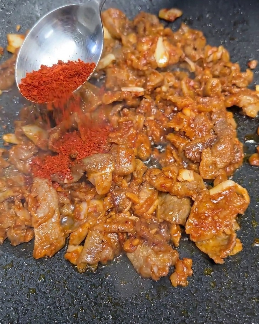 炒めた牛肉と味噌のベースに赤い粉唐辛子を加えている様子。