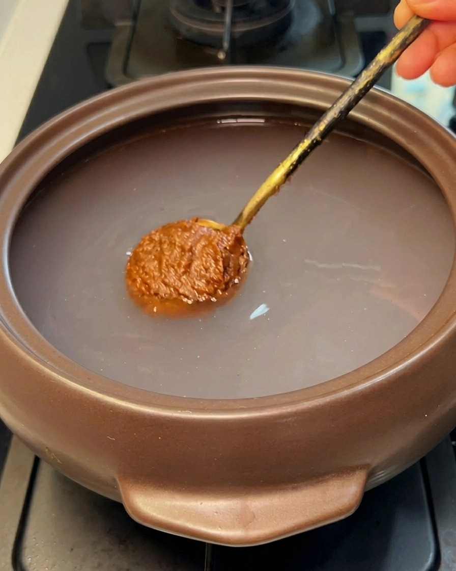 熱湯が入った石鍋に、スプーン一杯の韓国味噌を溶かし入れている様子。