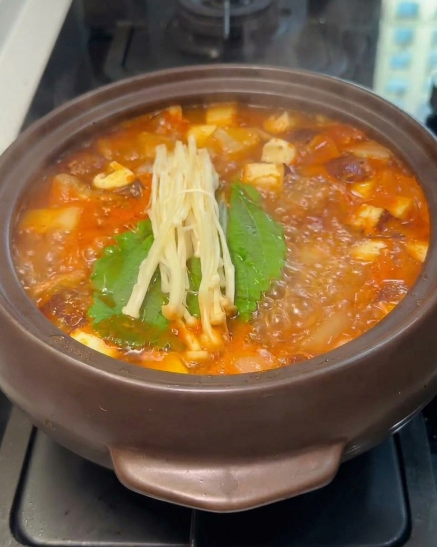 赤いスープの中、葉物野菜の上にえのき茸がのっている様子。