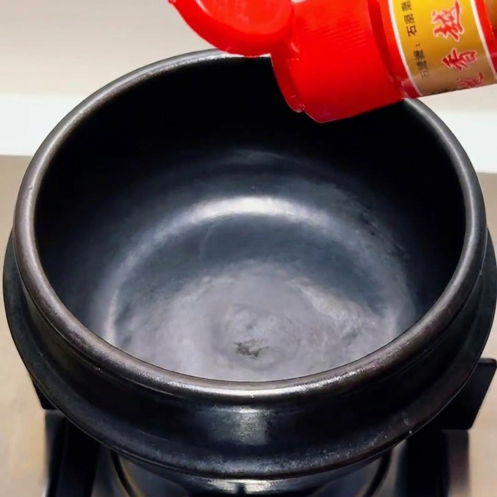 赤色のキャップのボトルから黒い土鍋にごま油を注いでいる様子。