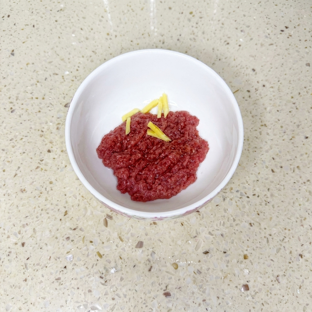 ボウルに入った牛ひき肉に醤油、油、片栗粉を加え、生姜のスライスを添えた状態。