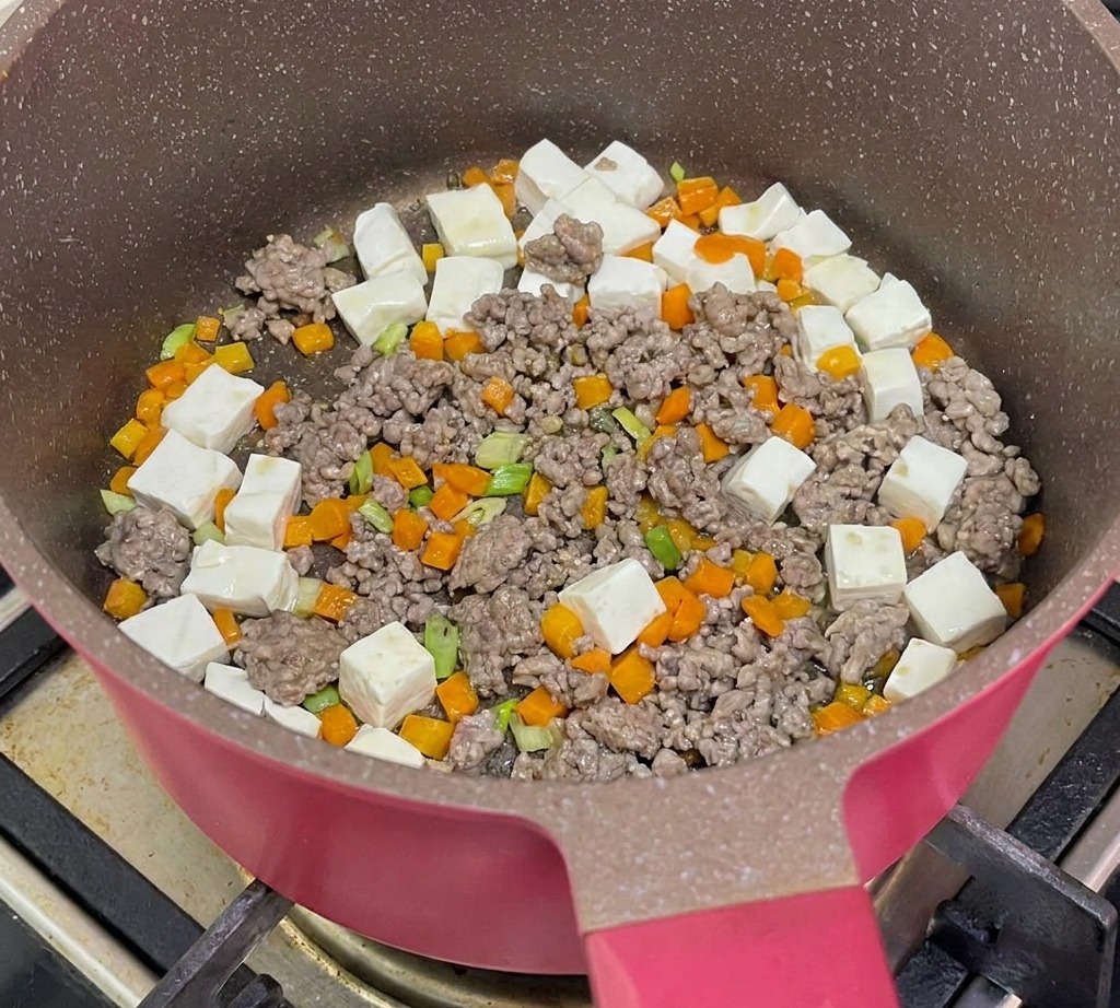 食材が入ったフライパンに熱湯を注ぎ、煮込んでいる様子。