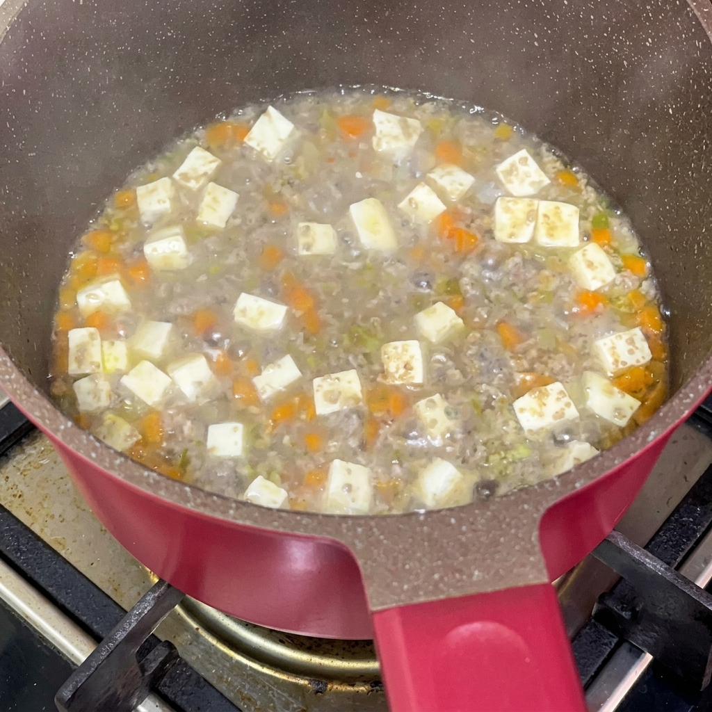煮込んでいる鍋に醤油を回し入れている様子。