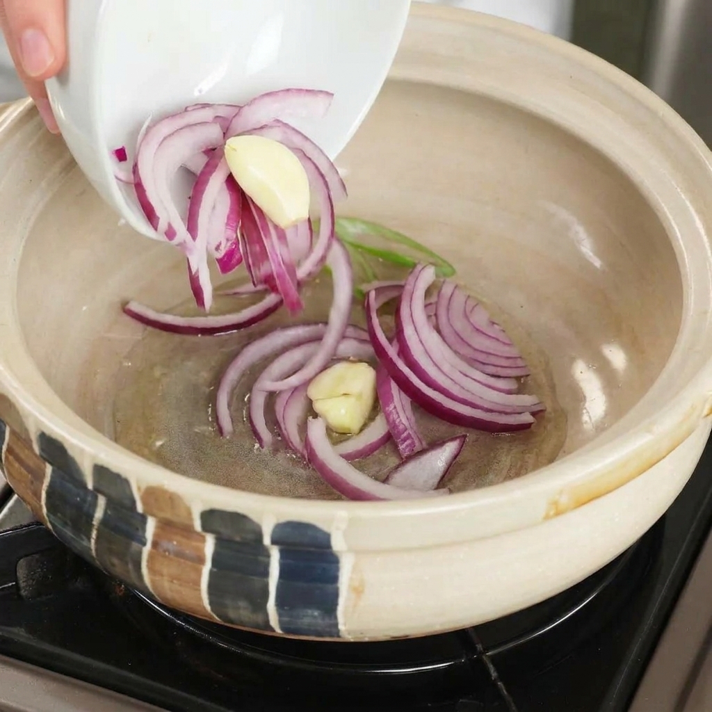 熱した土鍋で赤玉ねぎとにんにくを炒めている様子