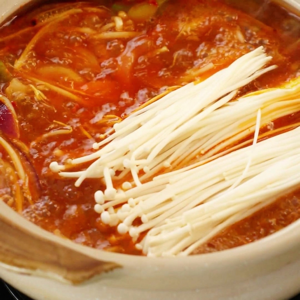 ぐつぐつと煮える赤いスープにえのきと豆腐を入れる様子