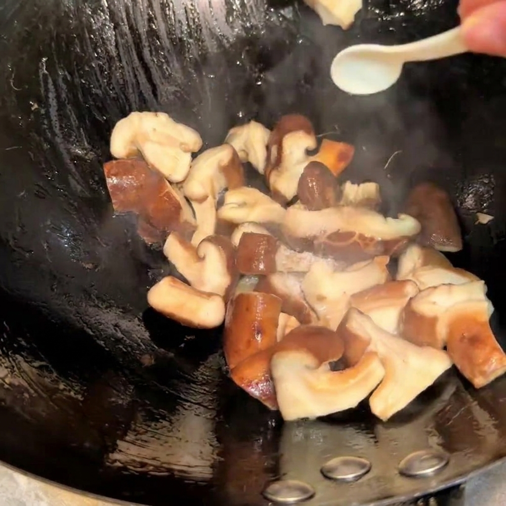 中華鍋の中で炒めている椎茸に、小さなスプーンで塩と醤油を加えて味付けしている様子。