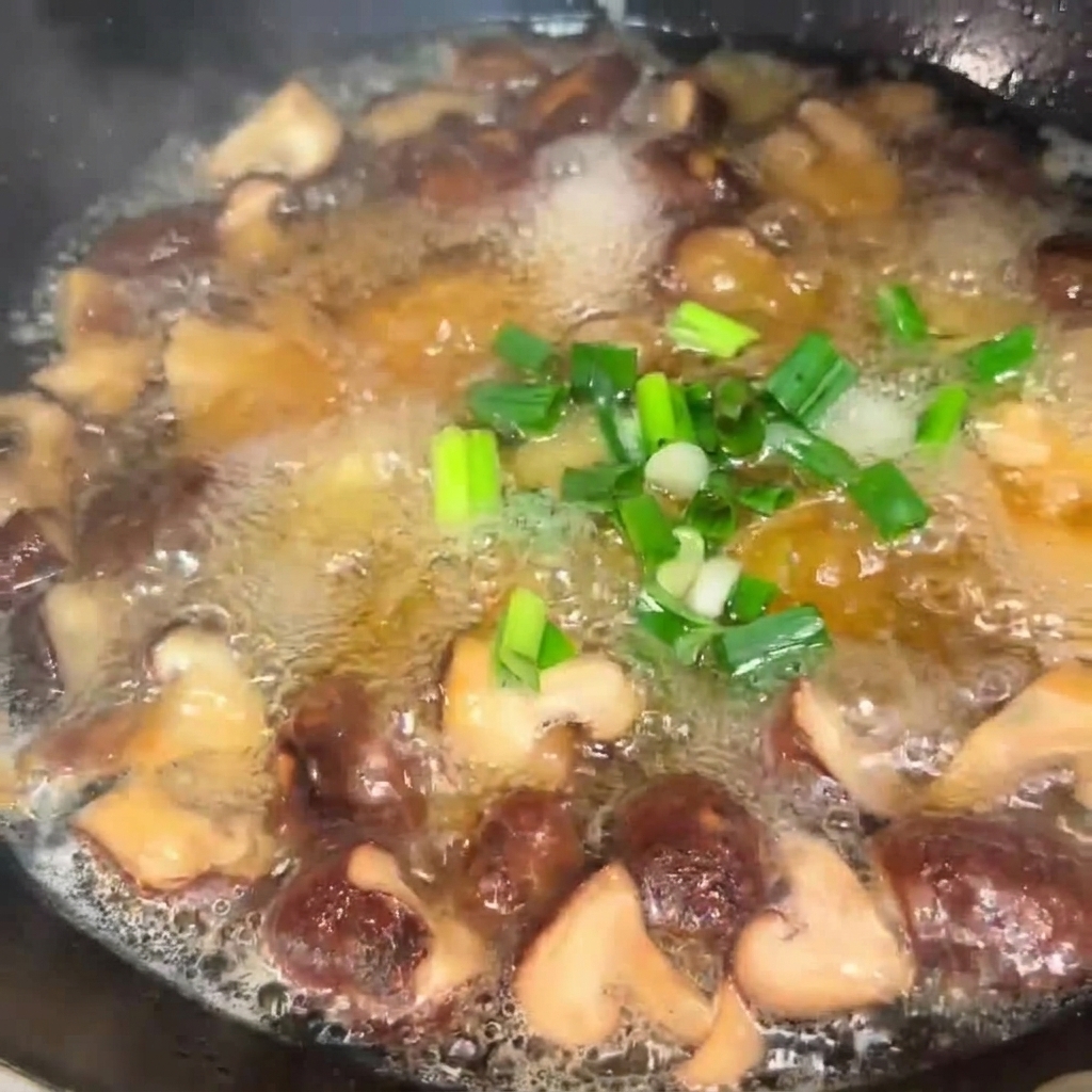 グツグツと煮えている椎茸と豆腐のスープに、刻んだネギを散らしている様子。