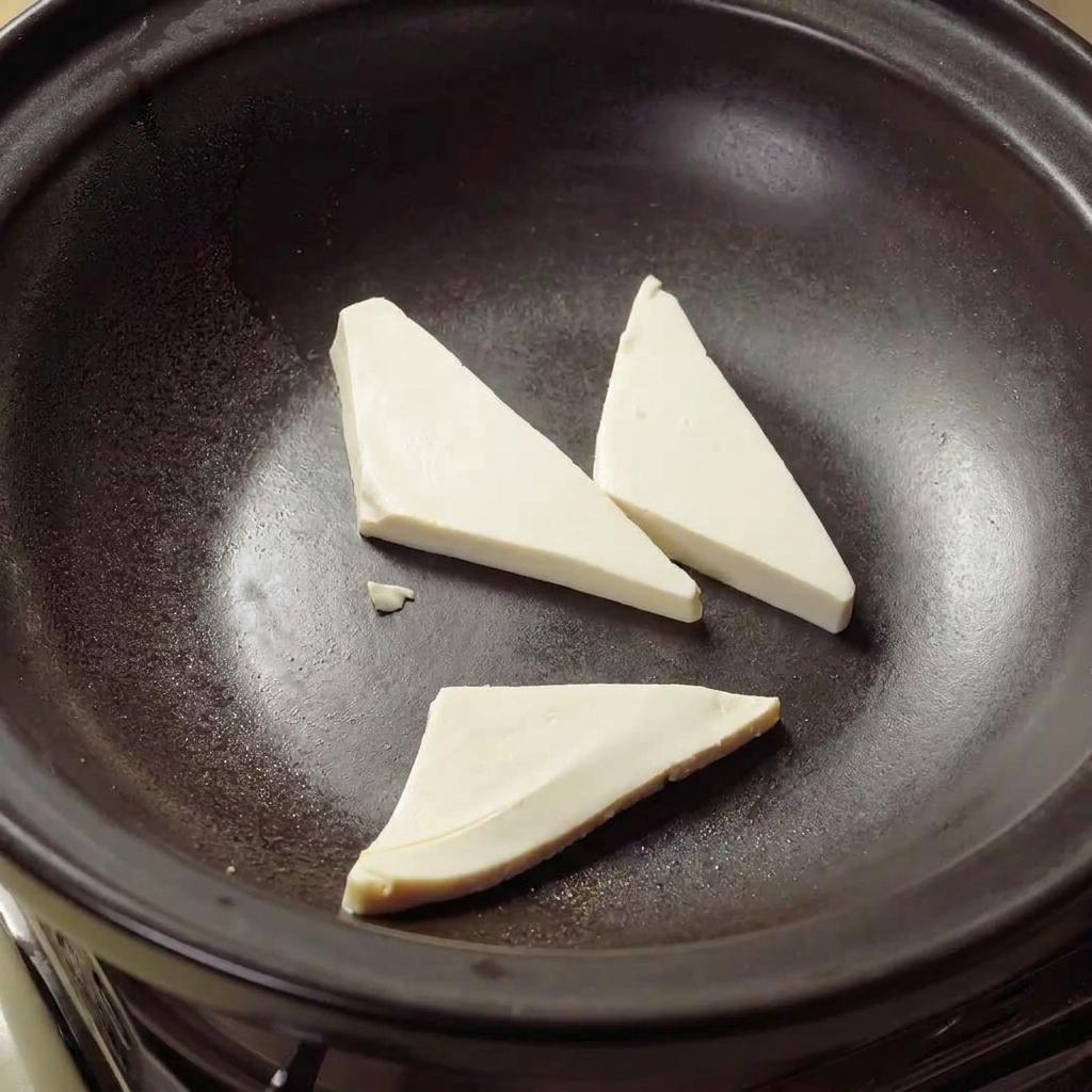 土鍋の中で豆腐の三角形が熱い油で黄金色に焼かれている様子。