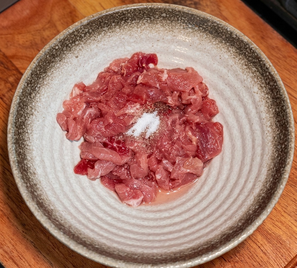 ボウルに入った豚肉に調味料と片栗粉を振りかけている様子。