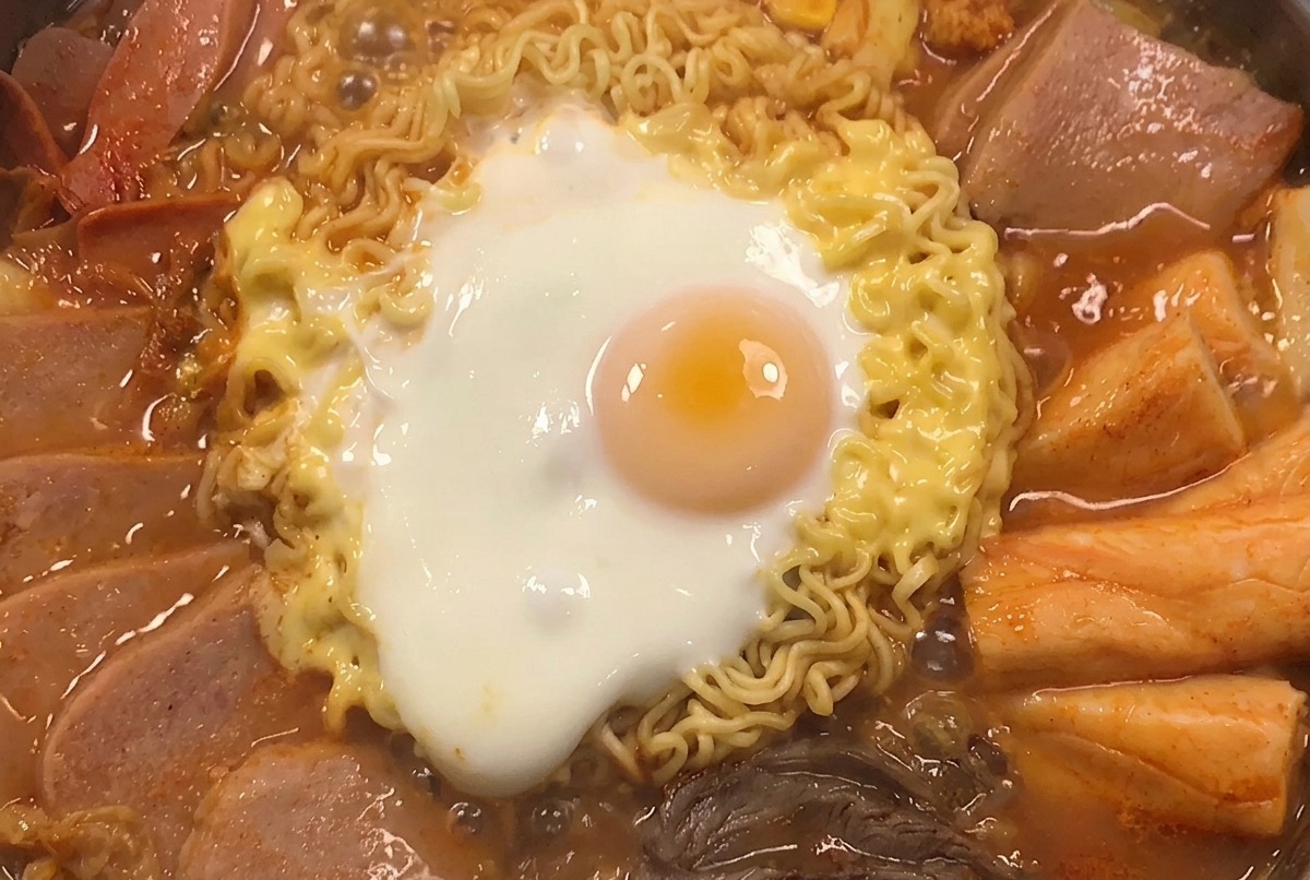 完成したプデチゲにスイートコーンと青ねぎをトッピングしている様子