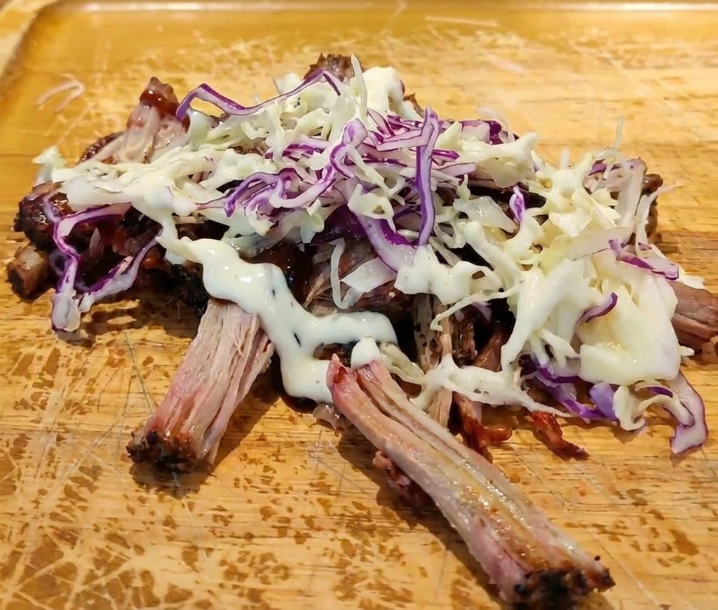 BBQソースを和えた豚肉と新鮮なコールスローの上に、白いクリーミーなドレッシングをかけている様子。