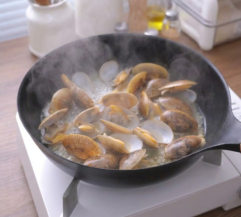 蓋を開けたフライパンから湯気が立ち上り、あさりがきれいに開いている様子。