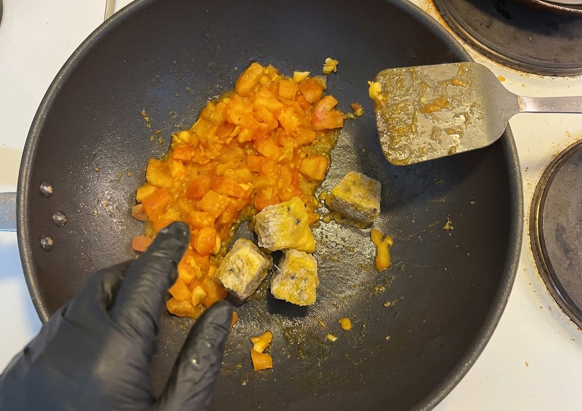 炒めたトマトが入った鍋に、冷凍のパッションフルーツ果肉と刻んだ唐辛子を加える様子。